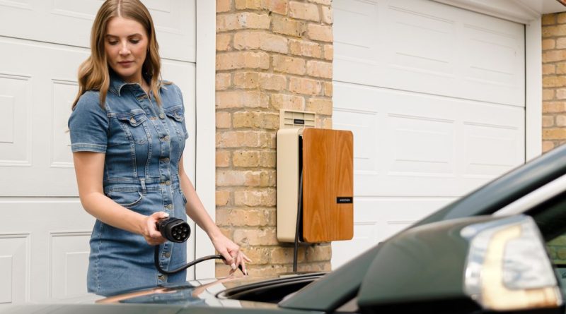 Persona sostiene el conector de recarga junto a un coche eléctrico y cargador doméstico; imagen ilustrativa